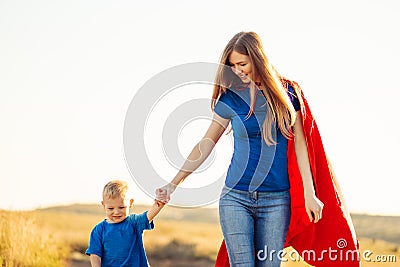 Super mom and her son walk forward holding hands. Cheerful family, a woman in a red raincoat as a superhero Stock Photo