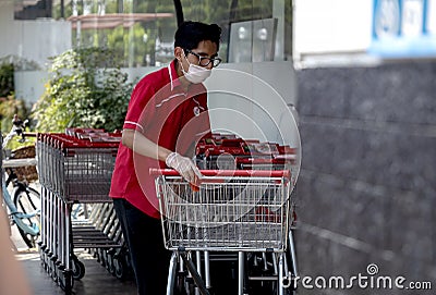 Supermarket worker disinfecting shopping carts and wearing a mask Editorial Stock Photo