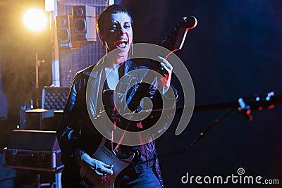 Superstar woman standing in front on microphone while playing at electric guitar working at rock album Stock Photo