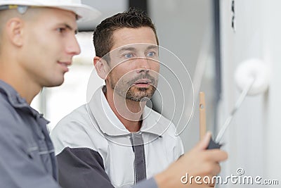 Supervisor watching apprentice painter use roller Stock Photo