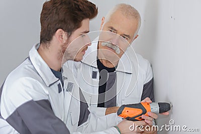Supervisor watching apprentice use drill on interior wall Stock Photo