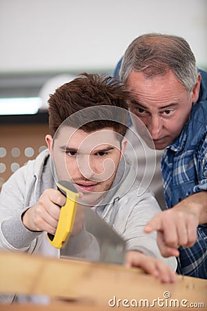 supervisor watching apprentice use handsaw Stock Photo