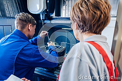 Supervisor watching young worker changing setup of lathe machine Stock Photo