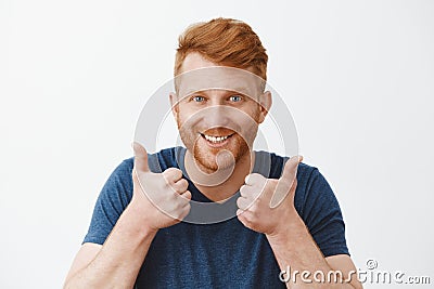 Supportive and attractive adult redhead male with bristle liking great plan raising hands, showing thumbs up, smiling Stock Photo