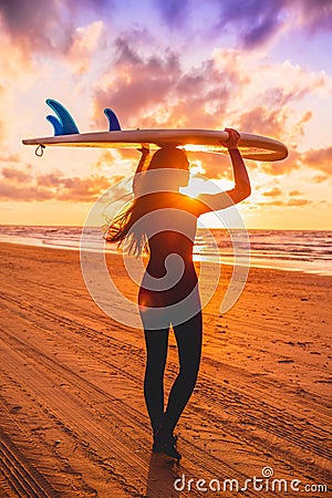 Surf girl with long hair go to surfing. Young woman with surfboard on a beach at sunset. Stock Photo