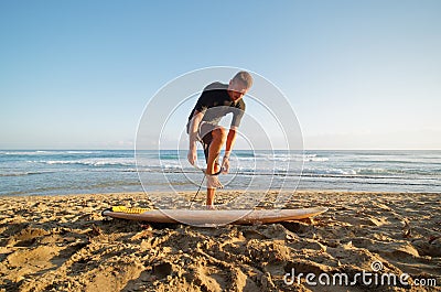 Surfer fastens leash at leg, going to surf in ocean at morning time. Stock Photo