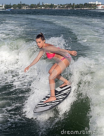 Surfer girl rides wave with fuchsia bright bikini over blue water Stock Photo