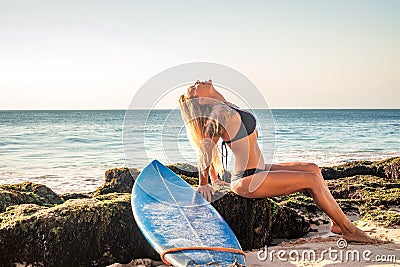 Surfer girl sitting on the rock. Blue longboard. Surfing lifestyle. Bali, Indonesia Stock Photo