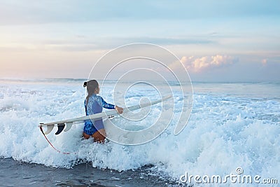 Surfer Girl. Surfing Woman With Surfboard Going To Surf In Ocean. Brunette In Blue Wetsuit Walking Into Splashing Sea. Stock Photo