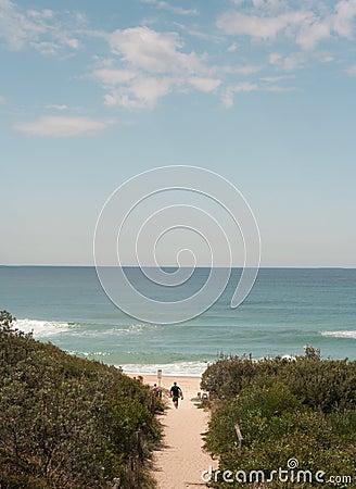 Surfer heading down path to surfing beach Stock Photo