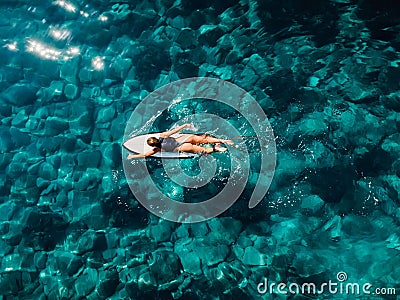 Surfer woman rowing on surfboard in turquoise ocean. Aerial view with surfgirl Stock Photo