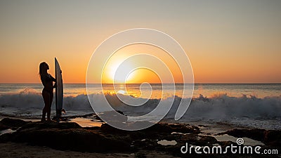 Surfing lifestyle. Silhouette of surfer girl with surfboard on the beach. Golden sunset time. Bali, Indonesia Stock Photo