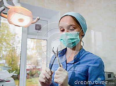 The surgeon dentist in mask holding forceps preparing for tooth extraction at clinic Stock Photo