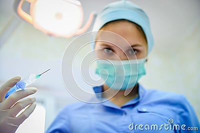 The surgeon dentist in mask holding syringe leaning over patient for injecting anesthesia Stock Photo