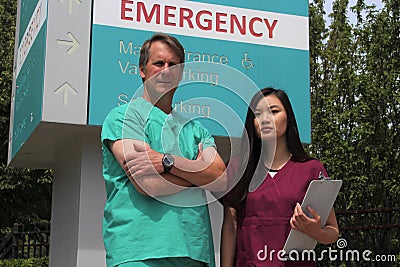 Surgeon or Doctor or Physician or Clinician and Asian Nurse Stand in Front of Hospital Emergency Room Sign Stock Photo