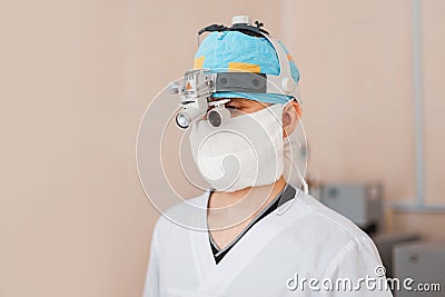 Surgeon man in a mask in special medical clothes wearing glasses with a binocular magnifying loupes is standing Stock Photo