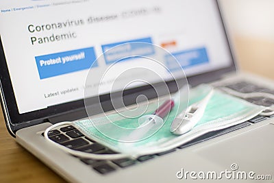 Surgical ear-loop mask, injection syringe and thermometer on the laptop Stock Photo