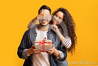 Surprise Present. Romantic young arab woman covering boyfriend's eyes and giving gift Stock Photo
