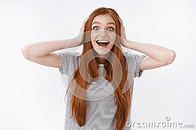 Surprised amazed excited cute young redhead girl wearing striped t-shirt widen eyes hold hands head impressed cannot Stock Photo