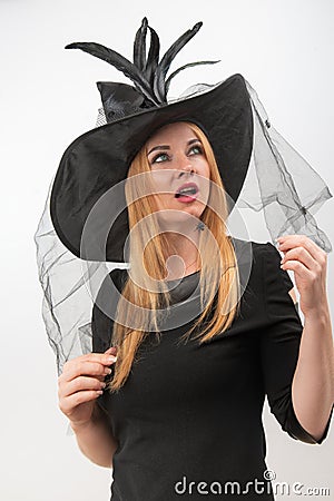 Surprised attractive blond woman in black witch hat with green eyes looks up. Young witch, vertical frame. Halloween party, white Stock Photo