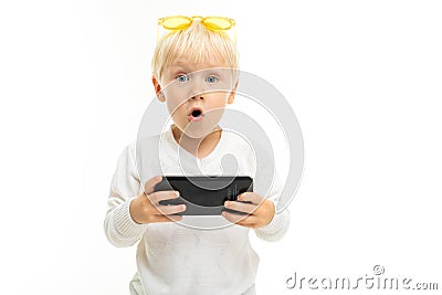 Surprised blond kid with a phone in a horizontal position in his hands on a white background Stock Photo