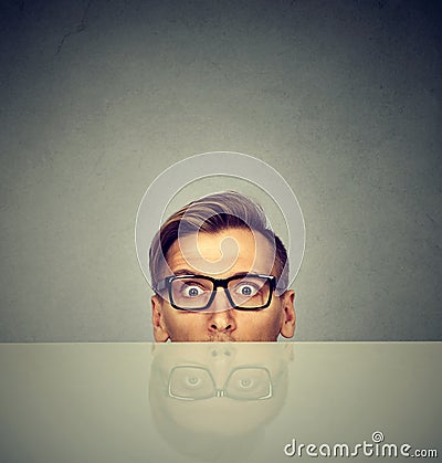 Surprised businessman peeking from under table Stock Photo