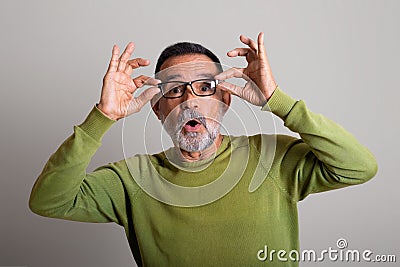 Surprised cheerful caucasian elderly man takes off glasses with open mouth on gray studio background Stock Photo