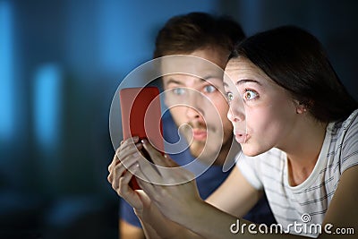 Surprised couple checking phone in the night at home Stock Photo