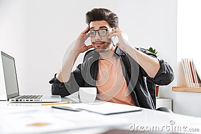 Surprised displeased handsome man in eyeglasses talking by smartphone Stock Photo