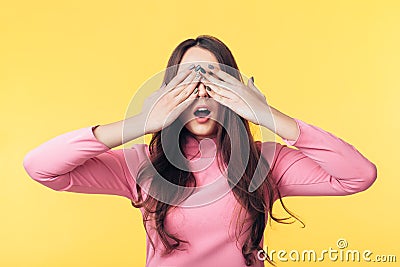 Surprised excited woman closed her eyes with hands waiting for surprise isolated on yellow background Stock Photo