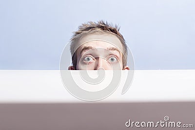 Surprised eyes of young man look out from behind the table. Voyeurism. Stock Photo