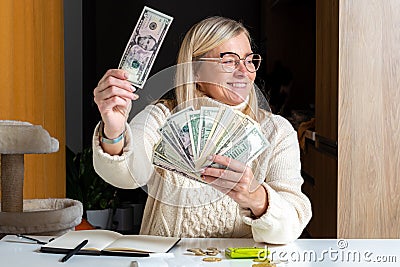 Surprised female employee sitting at work and looking at dollar banknotes, financial welfare concept Stock Photo