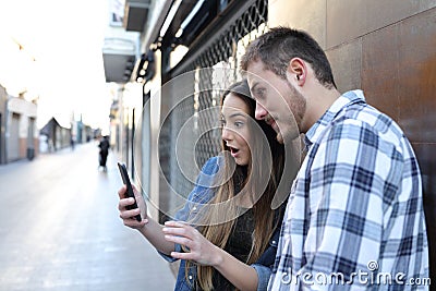 Surprised friends checking smart phone in the street Stock Photo