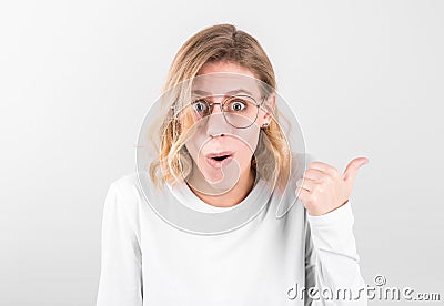 Surprised girl, keeps mouth opened, being stupefied as advertises something, , indicates with finger at upper right corner. Omg Stock Photo