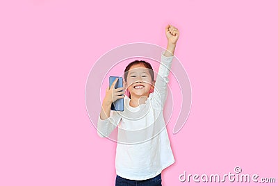 Surprised happy asian little child girl watching her smartphone and expression hand fight sign over pink background with copy Stock Photo