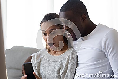 Surprised happy mixed race married spouse looking at smartphone screen. Stock Photo