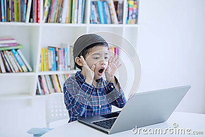 Surprised little boy using a laptop in the library Stock Photo