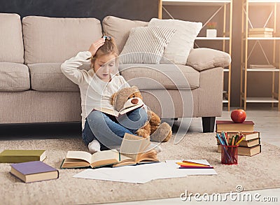 Surprised little female child hugging her teddy bear and reading Stock Photo