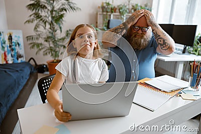 Surprised little girl does homework on laptop while father clutches head at home Stock Photo