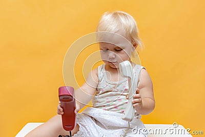 A surprised little girl holds a wired telephone receiver in her hands and does not know what to do with them Stock Photo