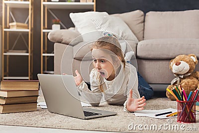 Surprised little girl doing homework on laptop, lying on floor Stock Photo