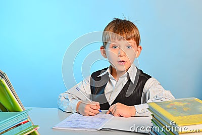 Surprised little schoolboy among notebooks and textbooks at his desk at school in the classroom Stock Photo