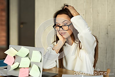 Surprised millennial girl scratches head at work Stock Photo