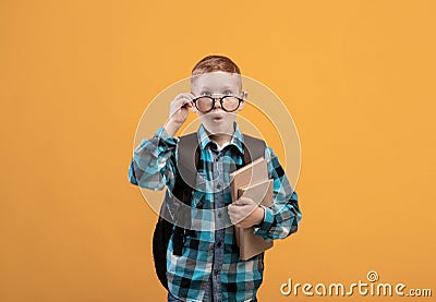 Surprised schooler with eyeglasses holding books on yellow background Stock Photo