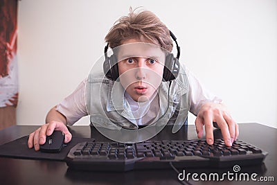 Surprised teenager in the headphones sits at home in the room behind and plays video games on a computer Stock Photo