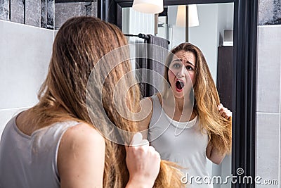 Surprised unhappy young woman checking her dry tousled long hair Stock Photo