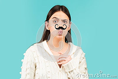 Surprised winking model Girl holding funny mustache on stick and showing empty copy space on open hand palm for text Stock Photo