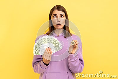 Surprised woman holding bitcoin and big fan of euro bills, exchange crypto currency. Stock Photo