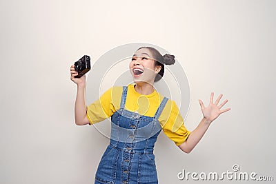 Surprised woman, with top knot hairdo, wearing on denim jumpsuit, holding retro camera, on the white background Stock Photo