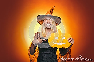 Surprised woman in witches hat and costume on red Halloween background. Attractive model girl in Halloween costume Stock Photo